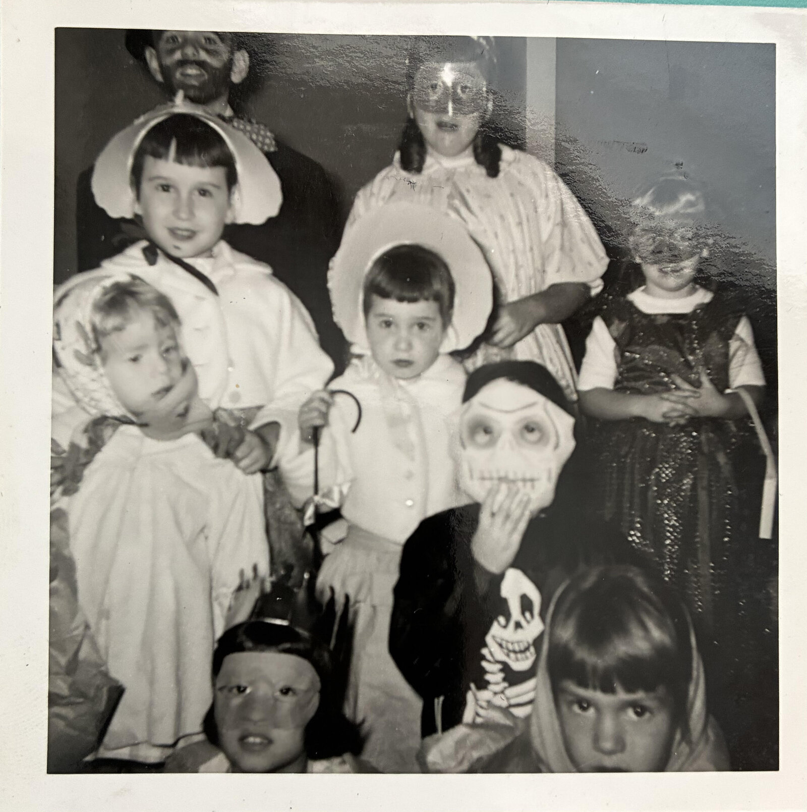 Vintage black-and-white photo of neighborhood kids in homemade 1950s Halloween costumes, including bonnets, masks and a skeleton
